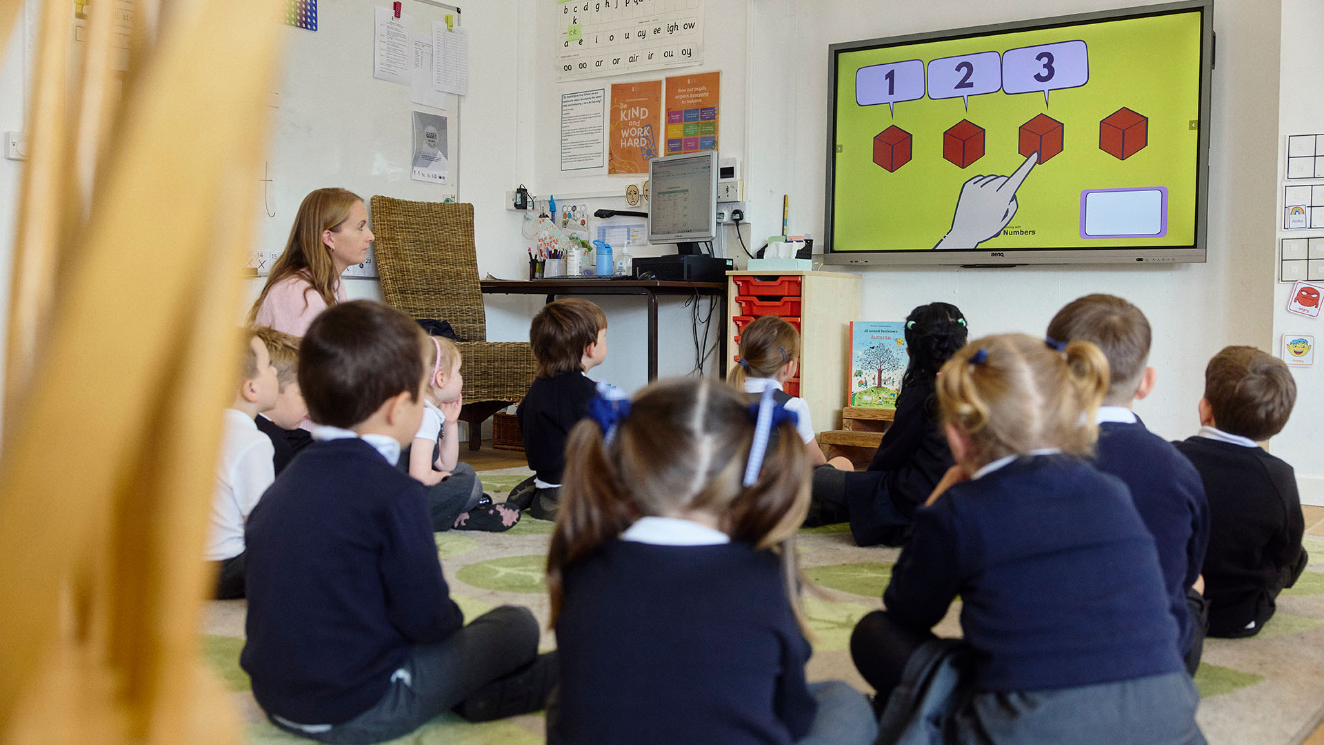 Teacher and pupils sat on carpet looking at interactive whiteboard