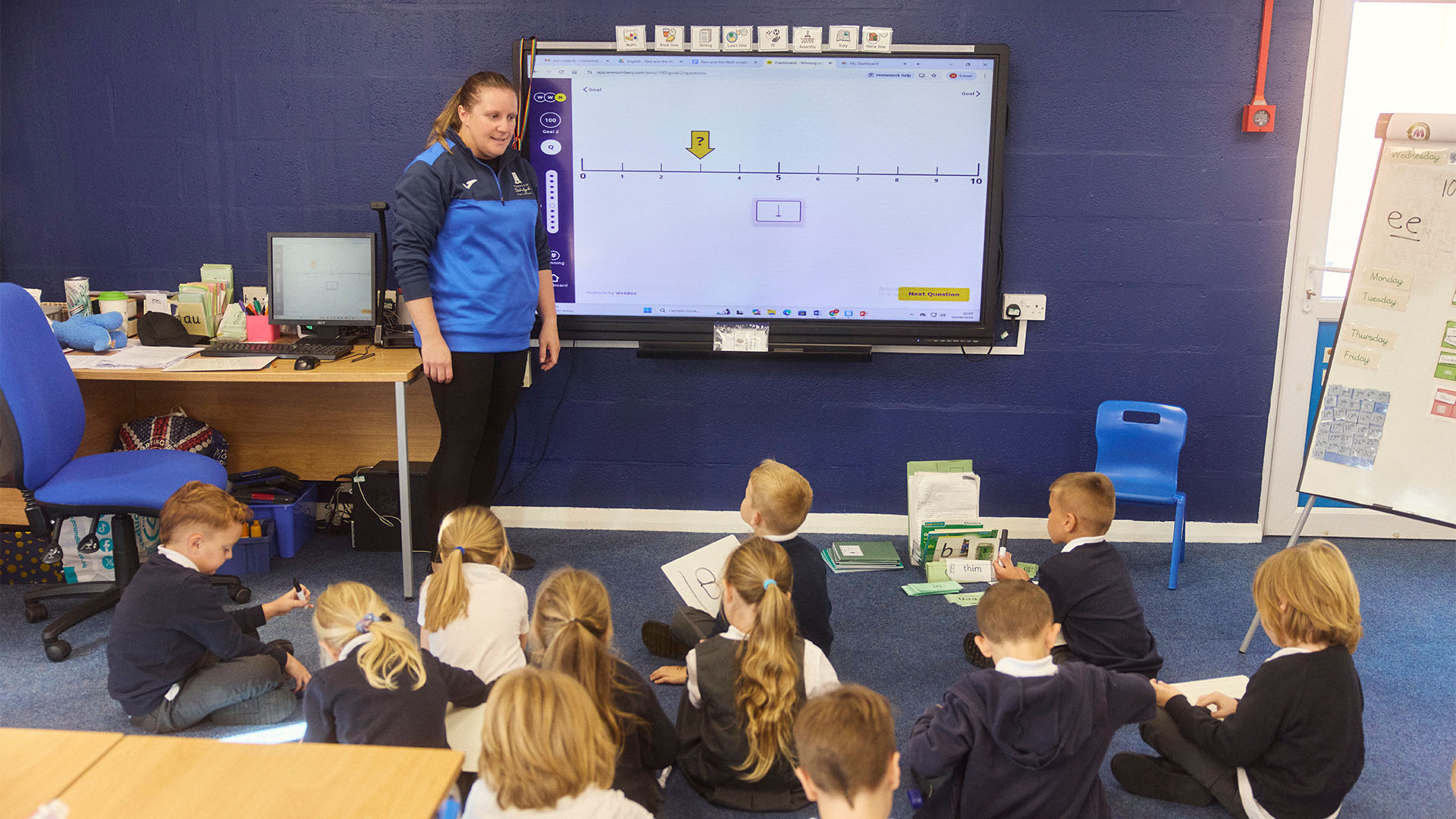 Teacher at whiteboard with pupils on the carpet