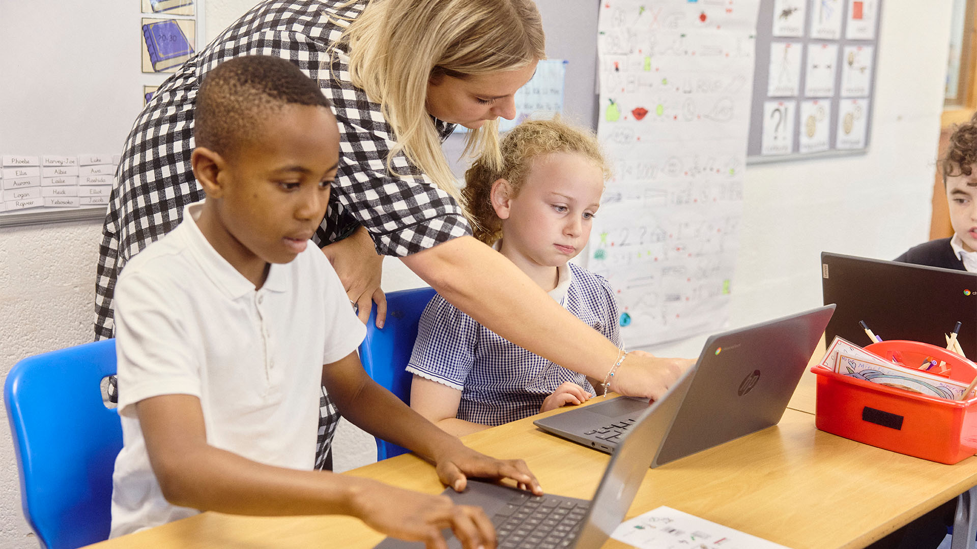 Two pupils at desks on laptops with teacher helping